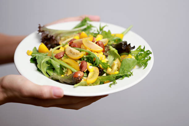Cropped image hands holding a plate of mixed salad. A multi-coloured healthy salad bowl with assorted fresh fruits and vegetables, lettuce, tomatoes, rocket and corn close-up