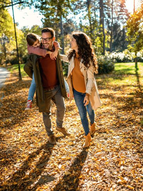 happy parents taking a walk with their little daughter in autumn - couple human pregnancy sunset walking imagens e fotografias de stock
