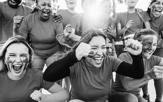 Multiracial sport fans screaming while supporting their team - Football supporters having fun at competition event - Focus on left girl face - Black and white editing