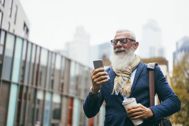 istock Business hipster senior man using mobile phone while walking to work with city in background - Focus face 1437682780