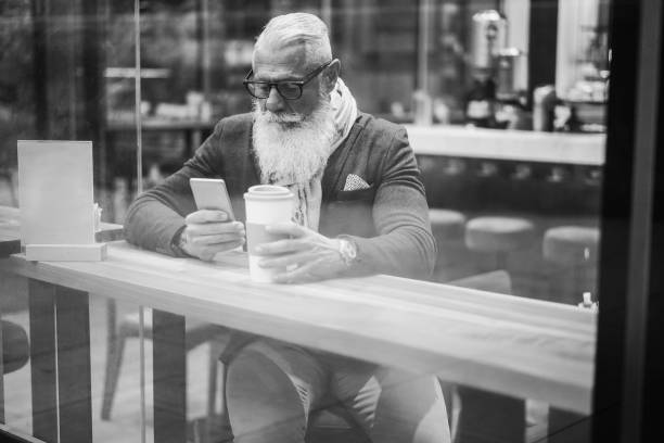 istock Senior business man using mobile phone while drinking coffee inside cafe bar - Soft focus on man eyeglasses - Black and white editing 1437682800