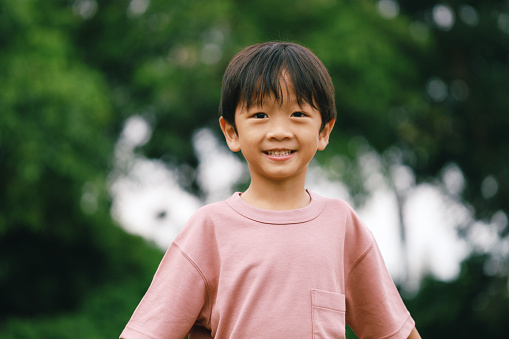A close up of a young Asian boy smiling at the park.
