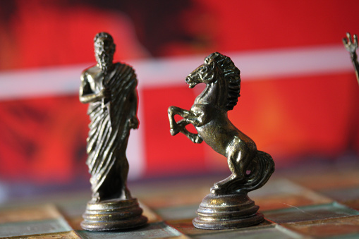 A closeup of Greek mythology chess pieces on the board with a red blurry background