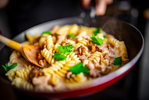 woman hand cooking tasty chicken fillet with mushroom in a creamy sauce with fusilli pasta in pan on kitchen