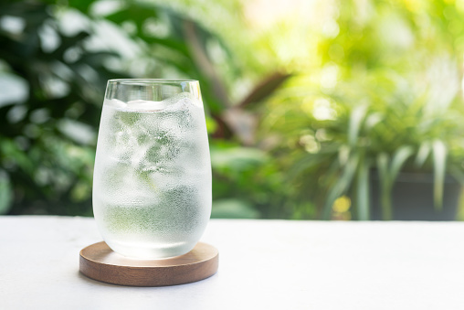A refreshing glass of ice water on bright green morning light background.