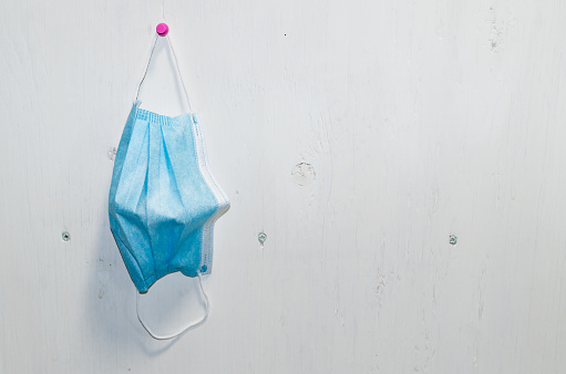 A closeup of a used disposable mask hanging on a white wall - precaution, disease control concept