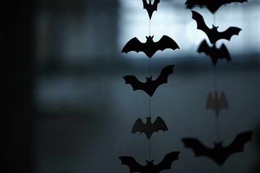 Black silhouettes of bats are vertically arranged on a blurred gray background. Garland for Halloween
