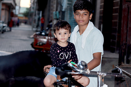 Teenage boy riding cycle with small baby girl outdoors in street.