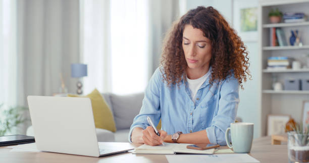 istock Freelance, laptop and notebook with a woman writing an idea on paper while remote work from home. Computer, internet and proposal with a female entrepreneur working at a desk in her house alone 1437694217