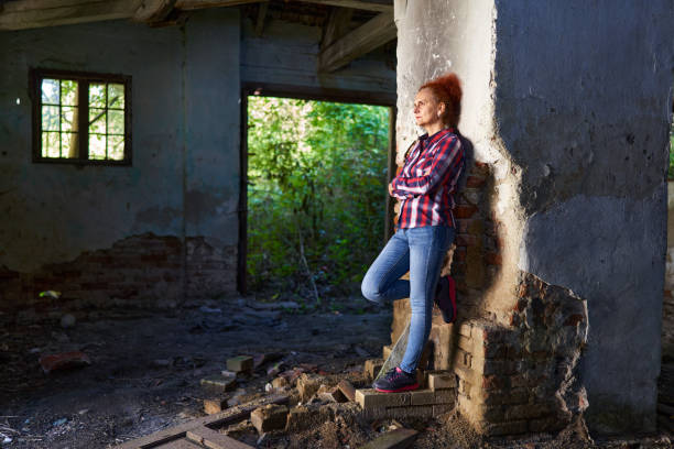 Curly haired redhead woman in plaid shirt and blue jeans in a ruined barn and house