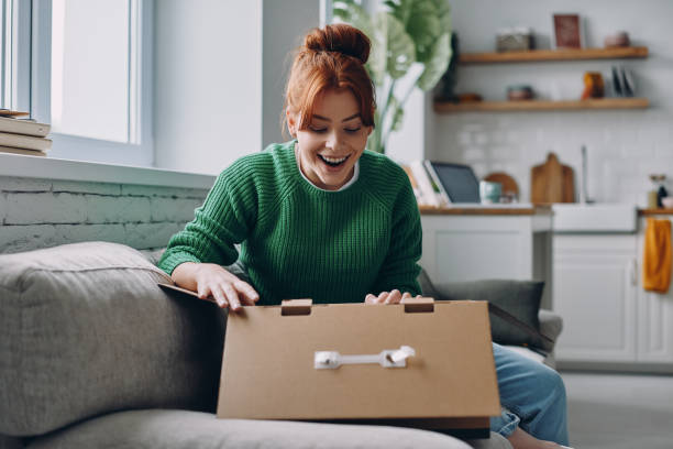 istock Happy young woman unpacking box while sitting on the couch at home 1437699723