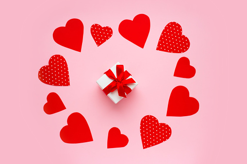 Paper red hearts around a gift box on a pink background. Happy Valentine's day concept. Valentine's day greeting card