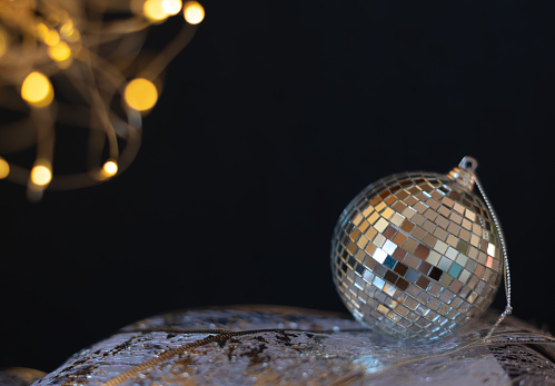 Silver disco mirror ball Christmas bauble close up with selective focus against black background. Xmas or winter holiday celebration concept. New Year greeting card with copy space for the text.
