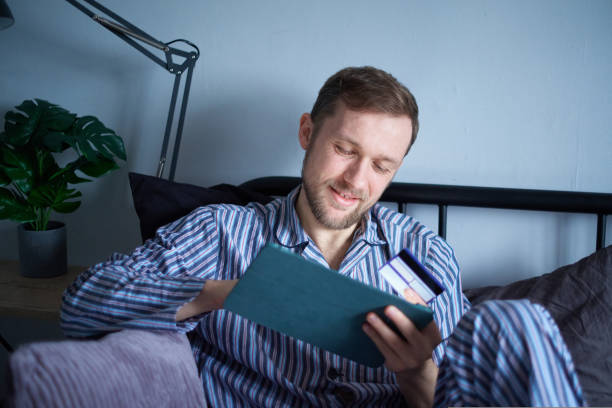 istock Male sitting on bed using tablet for shopping, purchasing with credit card 1437704817