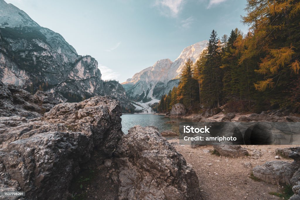 Mountain lake on cold morning in autumn Lake in the mountains in the dolomites at sunrise with rocks on the beach and larch trees on one side on sunny day in autumn Nature Stock Photo