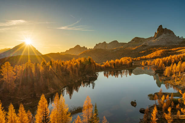 Sun rising behind mountain peak at Lake Federa in the Dolomites stock photo