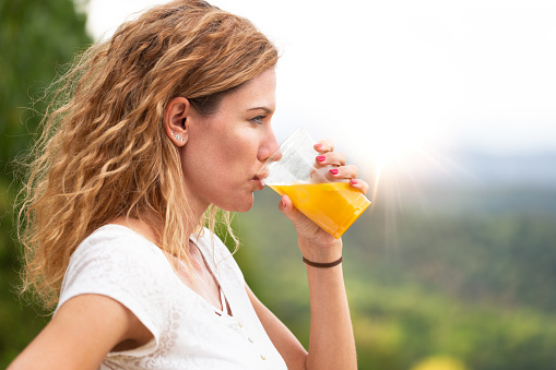 Young woman with curly hair drinking fresh juice at outdoors at morning, profile view