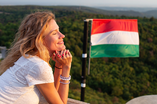 Young cheerful Caucasian woman relaxing in nature eyes closed, at Hungarian flag in sunset, Hungary