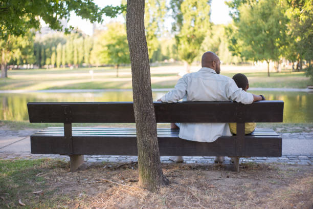 istock Back view of bearded African man and kid resting on bench 1437709925