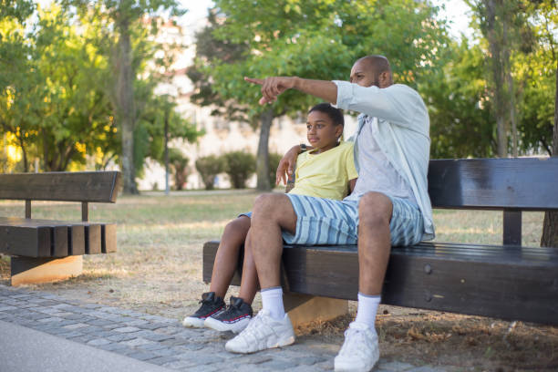 istock Side view of African American man hugging boy shoulder on bench 1437710257