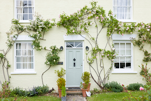 Buckinghamshire, UK - June 03, 2022. Home exterior UK. English house with green front door and wooden sash windows surrounded by climbing roses. England, UK