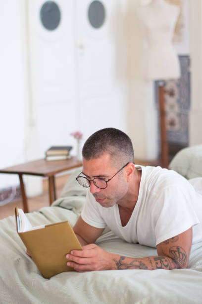 istock Focused man lying in bed in morning and reading book 1437713071