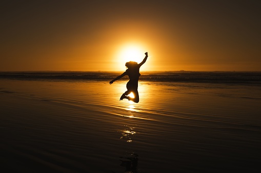 A silhouette of a young girl jumping on a beach at sunset in Oregon