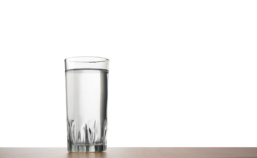 A glass of water standing on a table  isolated on a white background