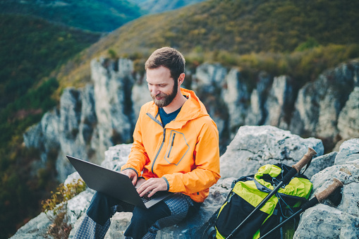 Hiker resting on the mountain top and using laptop