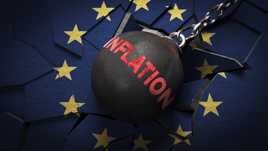 A wrecking ball crane  with inflation text hitting the wall covered with the European union flag