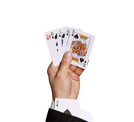 A hand of a man holding playing cards with an ace hidden on his coat