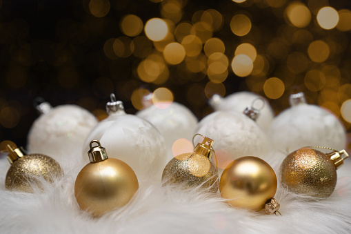 Festive christmas advent celebration holiday background banner greeting card - Collection of many golden and white modern christmas baubles, christmas balls on white soft fur with golden bokeh in the dark night, close-up