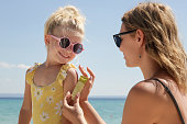 Mother applying sunscreen protection lotion on her cute little 4 years old girl, skin care during summer vacation