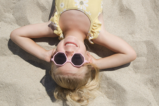 Happy little girl laying on the sand, top view