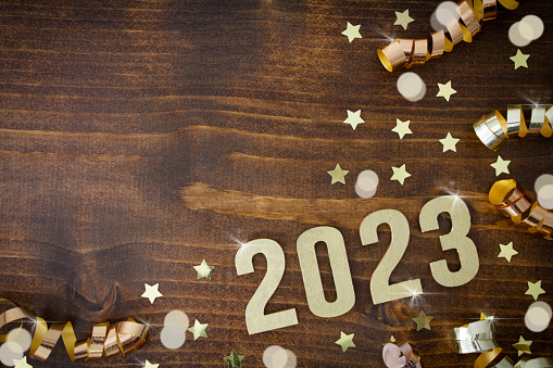 2023 written in gold on a wooden background with gold stars. ribbons and lights.\nWith copy space.
