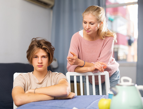 Mother and unhappy teenage son sitting after quarrel at home, mother consoles son