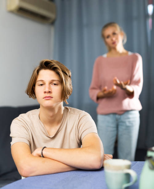 Portrait of unhappy son after discord with mother Frustrated teenage boy sitting at the table at kitchen after conflict with his mother brat stock pictures, royalty-free photos & images