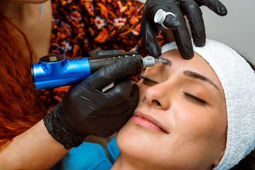 Beautician applying permanent make-up to beautiful woman's eyebrows