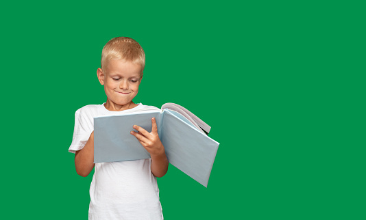 Boy looks in surprise at the open book. Green background with space for text. Selective focus. Picture for articles and advertisements about children, reading, education.