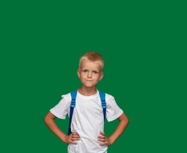 Boy in white T-shirt with backpack holds his hands around his waist. Green background with space for text. Selective focus. stock photo