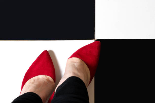 Selfie feet wears classic shoes court shoe on chequered floor background. Image legs in red velvet shoes pumps on black and white floor. Top view