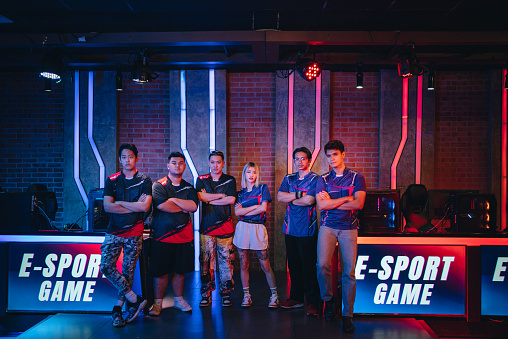 Asian Esports grand final team standing in front of stage with projector screen looking at camera with confidence look.
