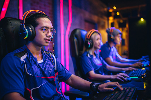 Pro gamer preparing for competitive MOBA computer game on a stage. Wearing headset and talking into the microphone to communicate with the pro team.