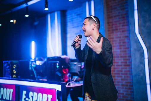 Asian male emcee game show host introducing grand final esports team players on stage.