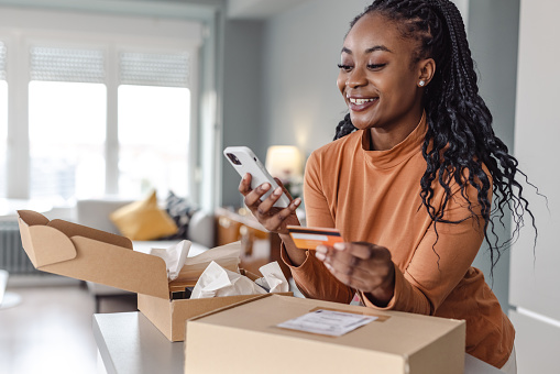 Portrait of excited African American female buyer holding credit card and using a mobile phone