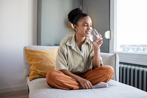 African American woman sitting on the couch and drinking a water. Concept of  hydration.