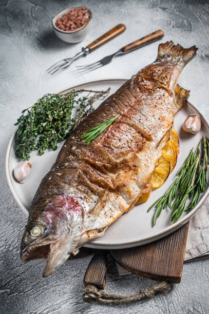 istock Baked silver trout, roasted fish on a plate with herbs. White background. Top view 1437740997