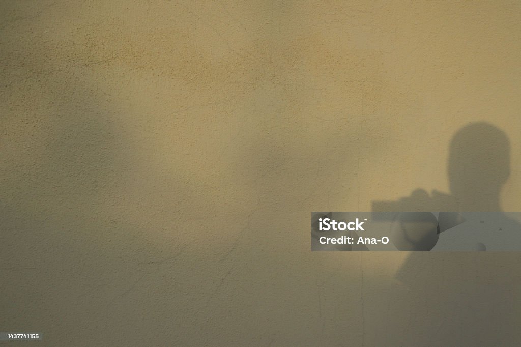 Shadows in a wall. Reflection / silhouette of the photographer taking photo of himself. Silhouette of photographer taking a photo Shadows in a wall. Reflection / silhouette of the photographer taking photo of himself. Black shadow silhouette of young man with photo camera Art Stock Photo