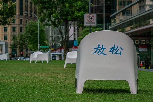 – August 03, 2022: White chair with 'Relax' written in Chinese in a public park at Raffles Place, Singapore.