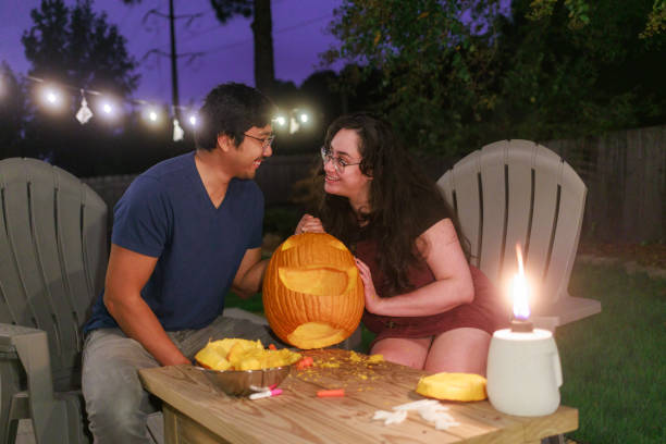 Couple Carving Pumpkins - Jack O'Lanterns - Halloween - Smiling at Each Other\nBack Yard
